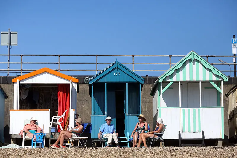 Foto av mennesker på strand med badehus i bakgrunnen